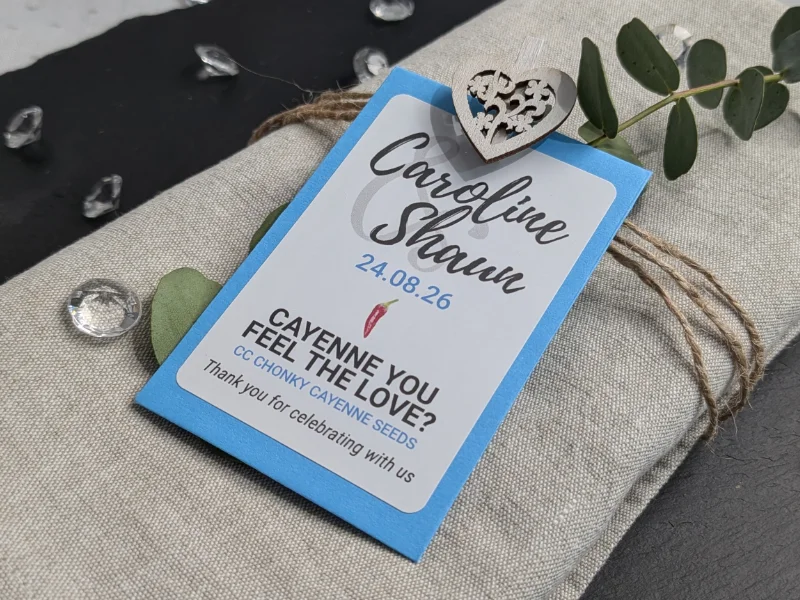 Chilli Wedding Favours: Handcrafted & Personalised 8 Wedding favour chilli seed packet with blue envelope and chilli pun, customised with bride and groom names and wedding date, displayed on a linen napkin with twine and eucalyptus