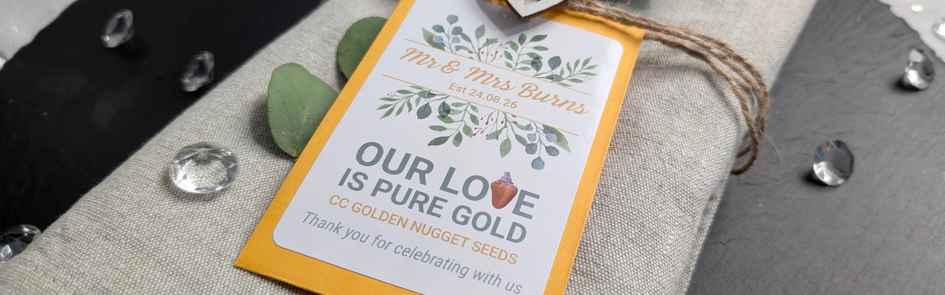 Chilli Wedding Favours: Handcrafted & Personalised 5 Chilli seed packet wedding favours with golden envelope sat on a linen napkin decorated with natural twine, eucalyptus and sparkly crystals on a slate placemat